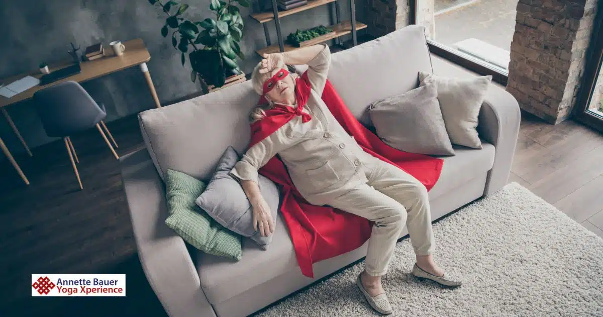 Ältere Frau mit Superheldenmantel und -maske sitzt erschöpft auf der Couch als Symbolbild wie du bei Herausforderung im Gleichgewicht bleiben kannst.